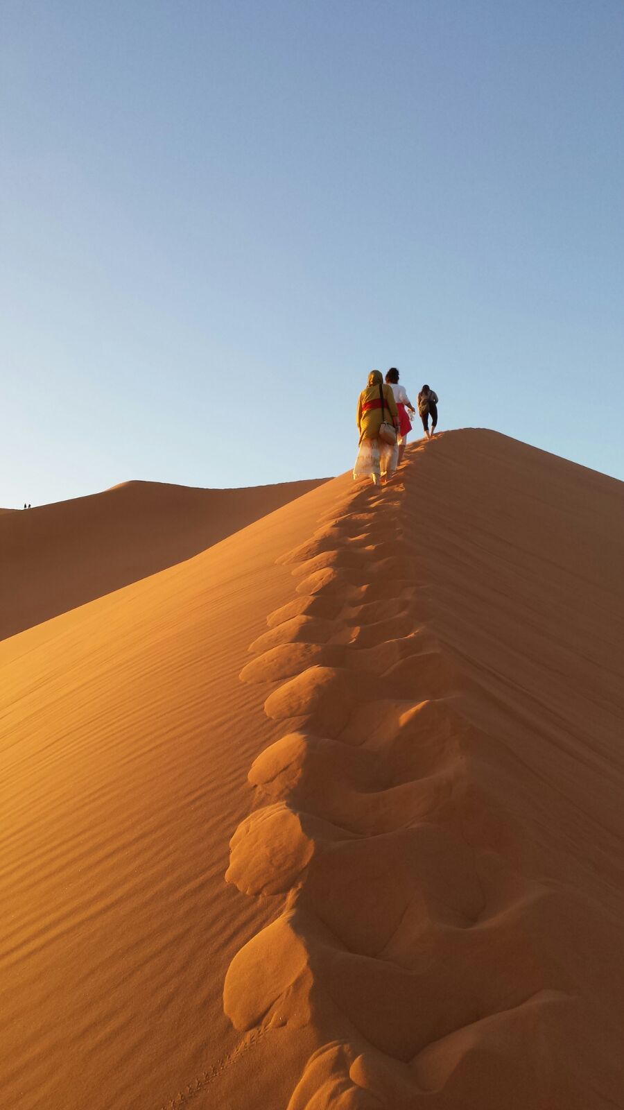 Yoga Wüstenreise, Menschen sitzen auf der Düne und schauen in den Sonnenuntergang
